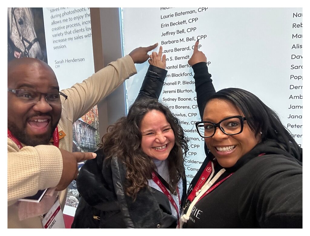 Three people are pointing to a name on a wall.